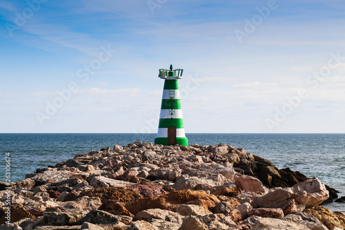 A green and white lighthouse at the end of a rocky pier photo
