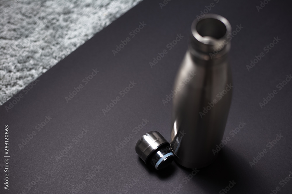 Steel thermo bottle for water with lid against black background.