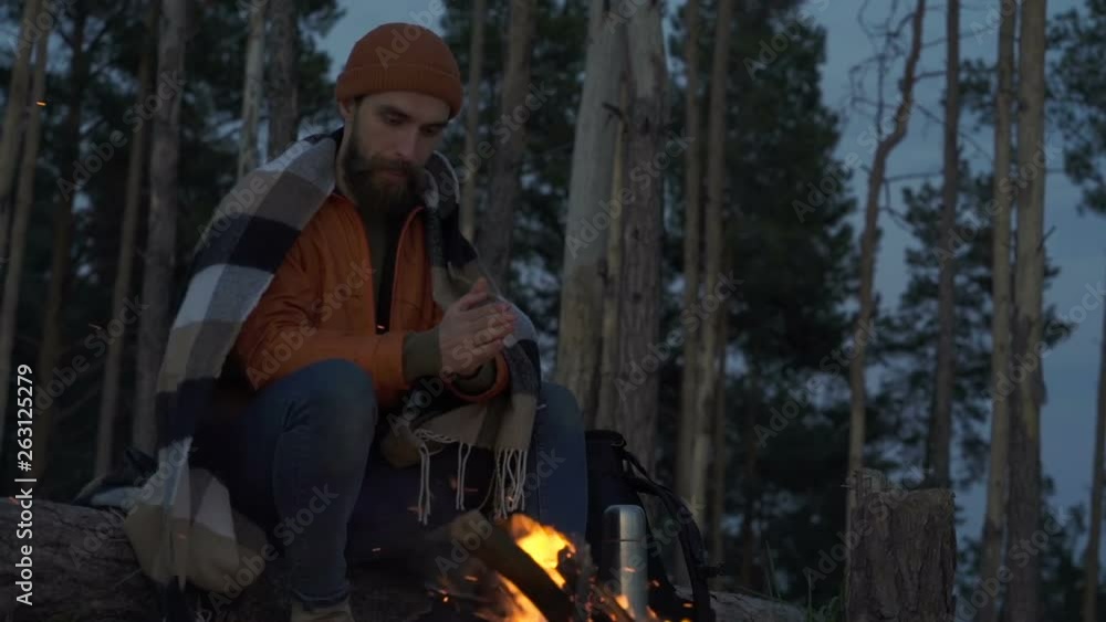 Man with plaid on him sitting near the bonfire and looking at it. Evening time. Man with plaid on him sitting near the bonfire and looking at it. Evening time.