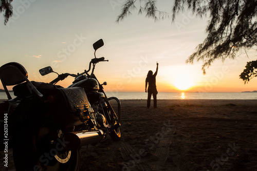 The young man stood on the beach. With a motorcycle parked He raised his hand to the sky. As if he had accomplished something