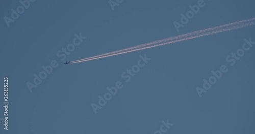 wide tracking shot of airplane with trails on clear blue sky in slowmotion