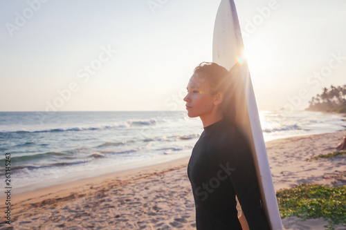 Young beautiful woman with a surfboard on the ocean with a surfboard in the rays of the setting sun
