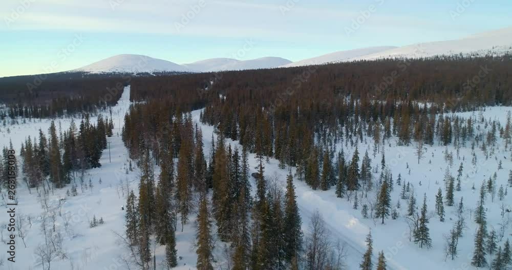 Aerial, reverse, drone shot, over spruce forest, buildings and Ounastunturit fjells, in Pallas-yllastunturi national park, at the arctic circle, on a sunny, winter evening, in Muonio, Lapland, Finland Aerial, reverse, drone shot, over spruce forest, buildings and Ounastunturit fjells, in Pallas-yllastunturi national park, at the arctic circle, on a sunny, winter evening, in Muonio, Lapland, Finland