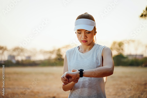 Woman runner looks at her watch checking her running time from smart watch. Athletic girl ready to run and looking at sport smart watch. Healthy runner checking performance.