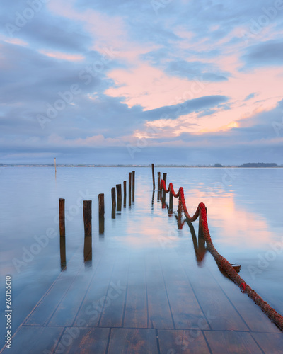 Palafitic pier submerged by the high tide at end of day, only the poles are visible. Blue hour witna tint of orange in the clouds.
