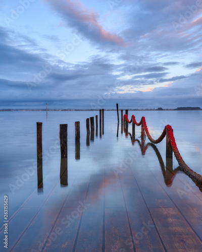 Palafitic pier submerged by the high tide at end of day, only the poles are visible. Blue hour witna tint of orange in the clouds. photo