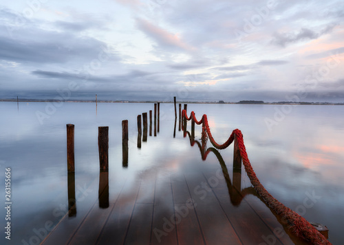 Palafitic pier submerged by the high tide at end of day, only the poles are visible. Blue hour witna tint of orange in the clouds. photo