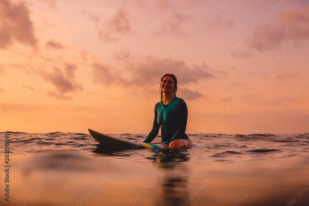 Surfer woman sit on a surfboard in ocean. Surfing at sunset