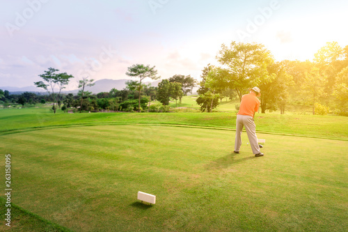 Male golfer teeing off golf ball from tee box on the Course to beautiful sunset