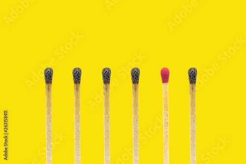 Business Idea and Leader Concept : New wooden match stick standing out from many burnt matches stick on yellow background.