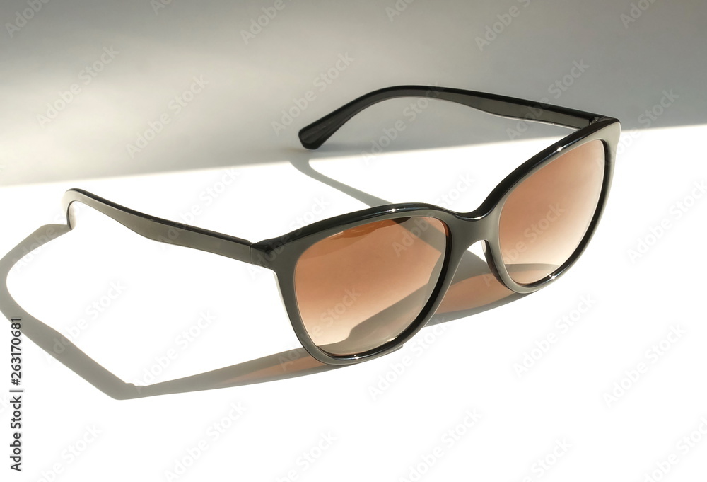 Black stylish sunglasses on a white background with sunlight shadows .copy space. creative concept Black stylish sunglasses on a white background with sunlight shadows .copy space. creative concept