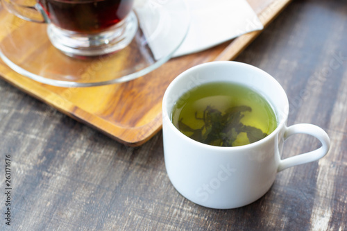 Green tea in teacup and black tea on wooden tray with tissue on wooden table. © Atiwan Janprom