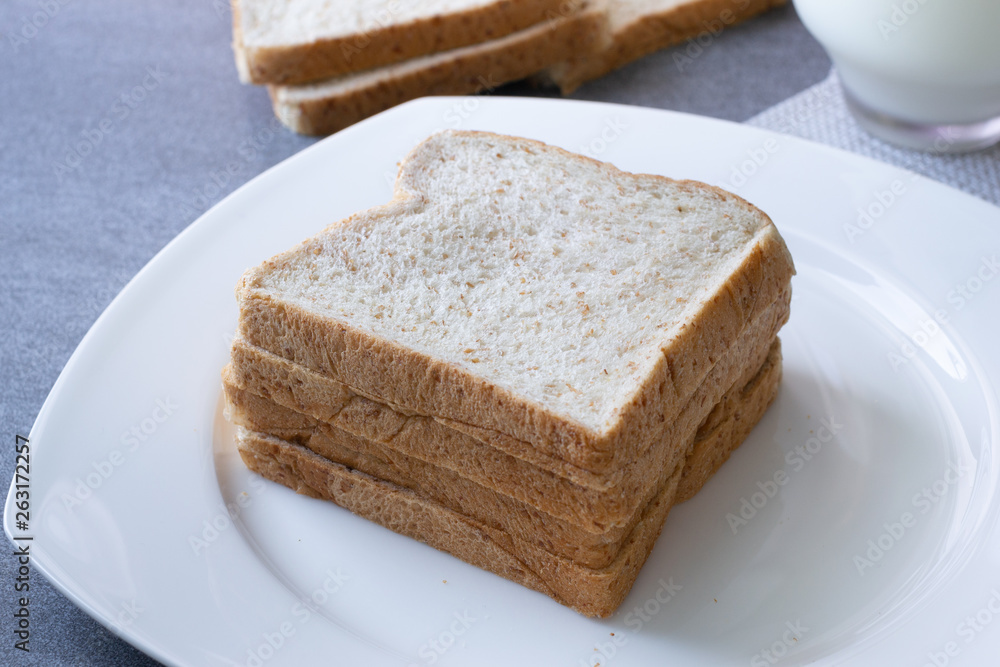 Whole Grain Bread in white dish and milk in glass on concrete table.