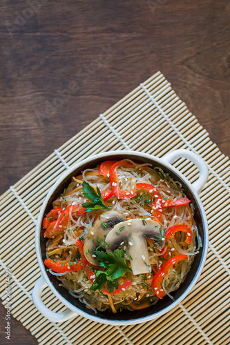Salad with glass noodles, mushrooms and various vegetables in a plate on a bamboo Mat on a brown table. Top view, close-up, copy space