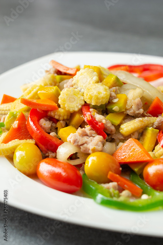 Stir fried vegetables with sweet pepper,tomato,pumpkin,corn and chicken in white dish on concrete table.