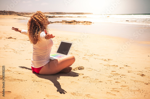 Happy free people caucasian woman sit at the ebach with computer laptop on her legs opening arms enjoying the freedom for vacation summer and for work free from stress office in the city photo