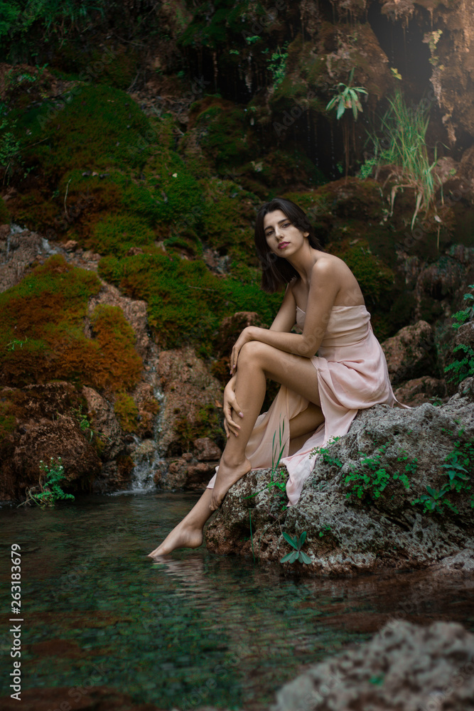 Fototapeta premium Beautiful girl posing in river. Fairytale story. Natural pool surrounded by green tree's leafs.