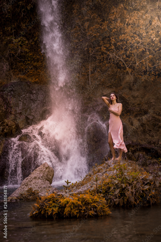 Attractive girl posing on the rock among in fairy fast forest in autumn and beside beautiful waterfall with blue water. Fairy tale. Attractive girl posing on the rock among in fairy fast forest in autumn and beside beautiful waterfall with blue water. Fairy tale.