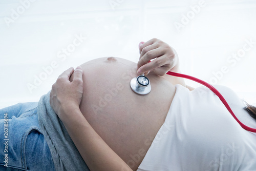 Portrait of Beautiful young pregnant women using stethoscope listening to her tummy.Pregnancy health care preparing for baby concept.Motherhood among teenage mother.