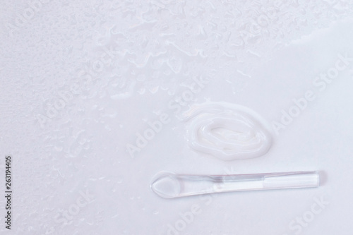 Cream, spatula for applying cream on a light background among water droplets