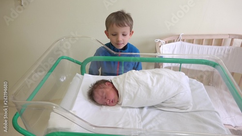 Obraz na płótnie Big brother looking to his newborn brother, baby sleeping in a bed in hospital