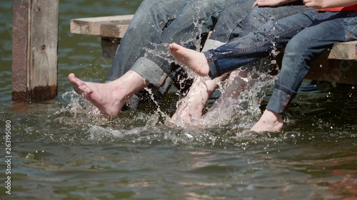 Slow motion detail of family feet playing in water while relaxing on wooden pontoon  child and parents feeling the joy of touching water