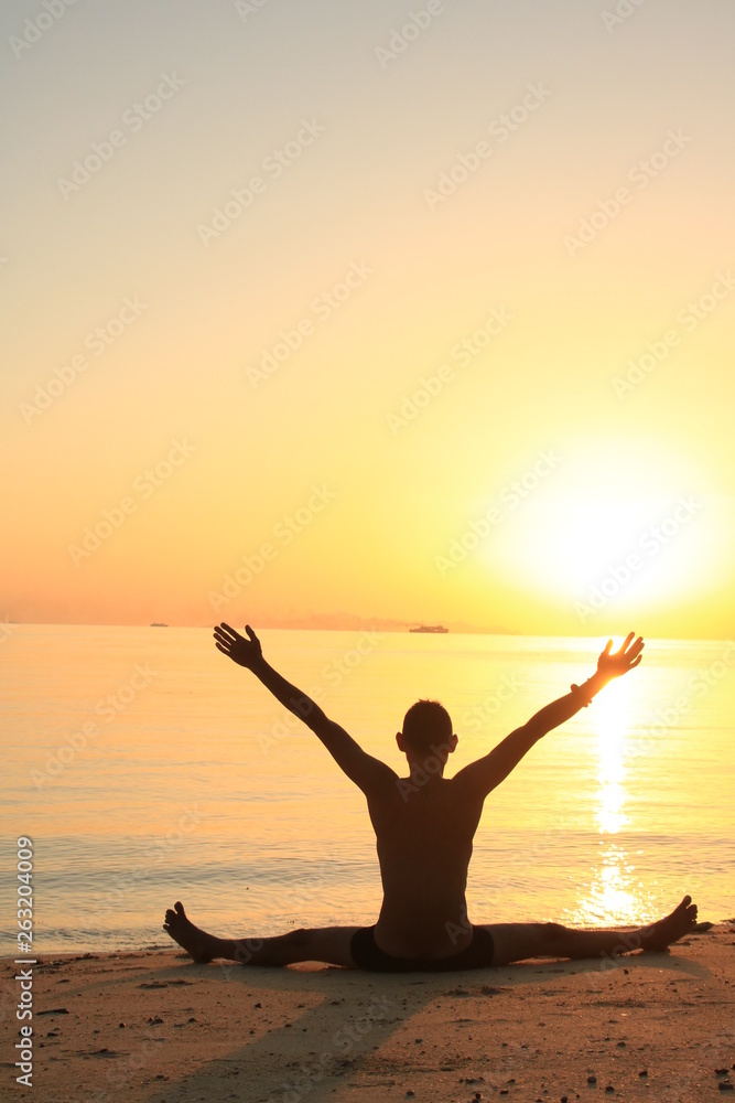 silhouette of young man practicing yoga on the beach at sunset