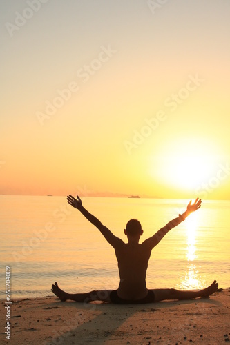 silhouette of young man practicing yoga on the beach at sunset © LI QING