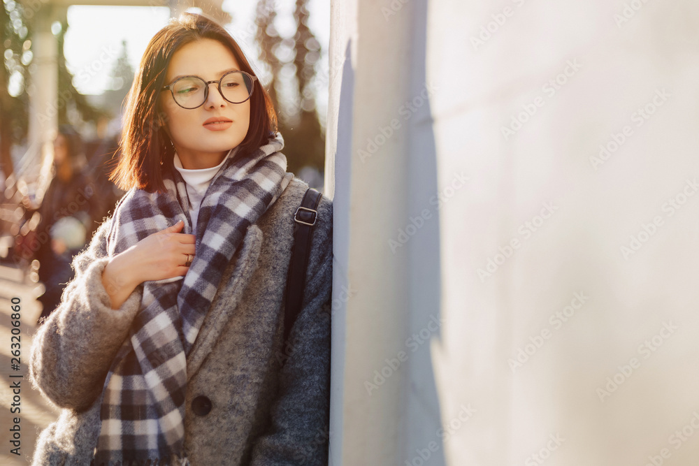 Fototapeta premium Attractive young girl wearing glasses in a coat walking on a sunny day