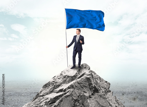 Handsome businessman on the top of the mountain with blue flag 