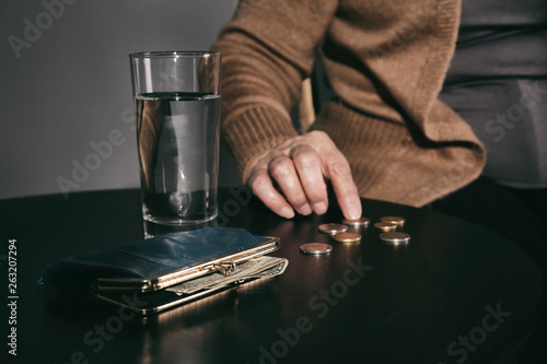 Poor senior woman with water, wallet and coins at table, closeup