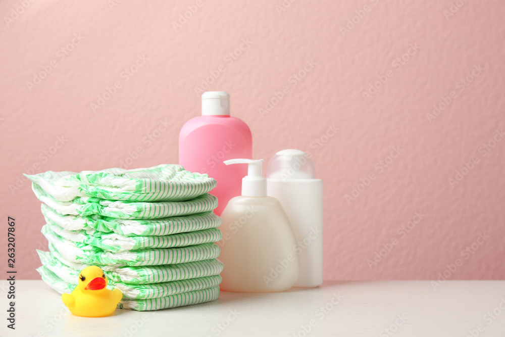 Stack of diapers, toiletries and toy duck on table against color background, space for text. Baby accessories Stack of diapers, toiletries and toy duck on table against color background, space for text. Baby accessories