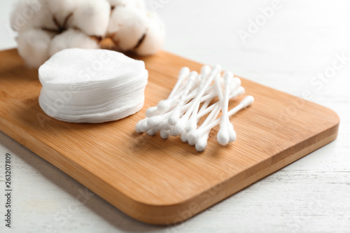 Board with cotton swabs, pads and flowers on white wooden background