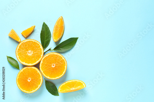 Fresh oranges and leaves on color background, flat lay with space for text. Citrus fruits