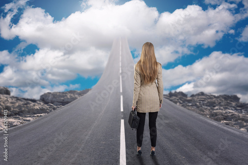 A businesswoman standing on road that goes up to the sky