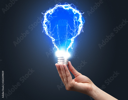 Hand holding shiny light bulb on dark background. New idea concept