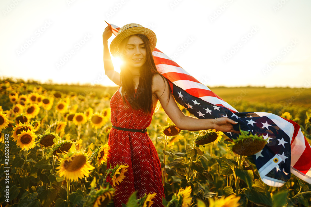 Beautiful girl in hat with the American flag in a sunflower field. 4th of July. Fourth of July. Freedom. Sunset light The girl smiles. Beautiful sunset. Independence Day. Patriotic holiday. Beautiful girl in hat with the American flag in a sunflower field. 4th of July. Fourth of July. Freedom. Sunset light The girl smiles. Beautiful sunset. Independence Day. Patriotic holiday.