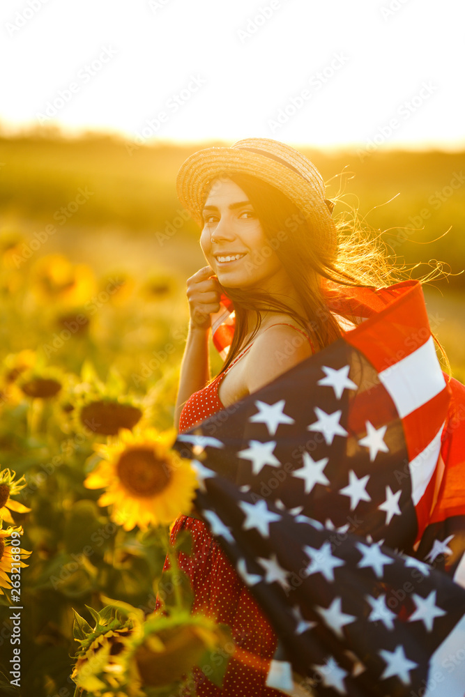Beautiful girl in hat with the American flag in a sunflower field. 4th of July. Fourth of July. Freedom. Sunset light The girl smiles. Beautiful sunset. Independence Day. Patriotic holiday. Beautiful girl in hat with the American flag in a sunflower field. 4th of July. Fourth of July. Freedom. Sunset light The girl smiles. Beautiful sunset. Independence Day. Patriotic holiday.