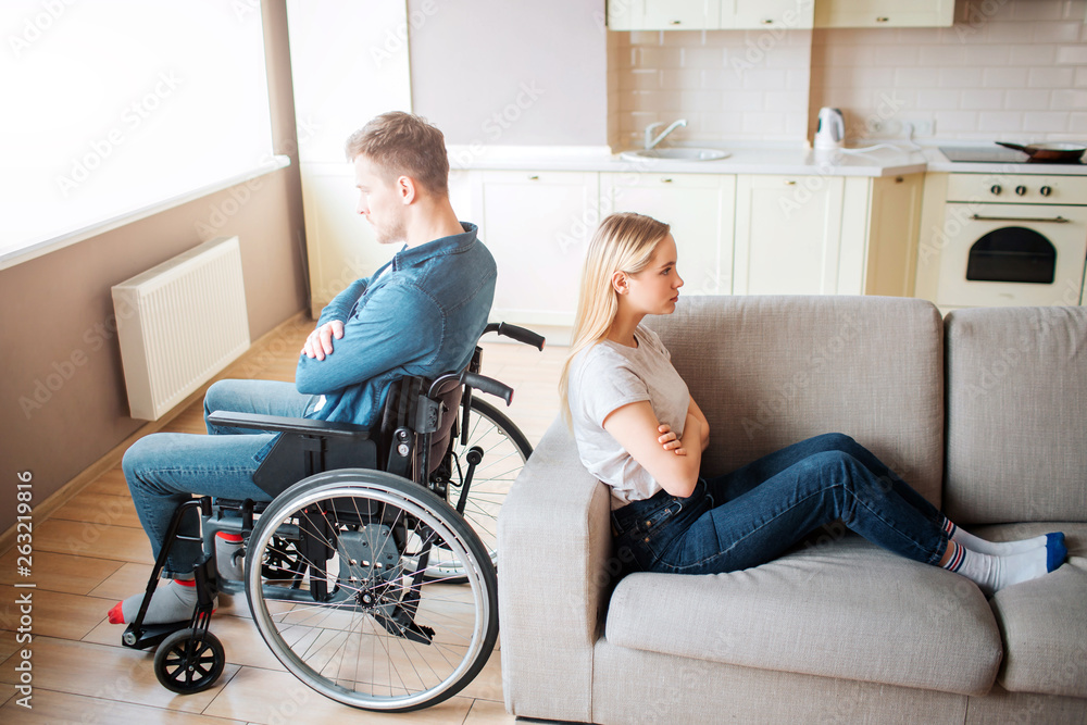 Young man with special needs and healthy woman sit back to back in room. Argue and quirrel. Worker with disability and inclusiveness. Upset and unhappy couple. Young man with special needs and healthy woman sit back to back in room. Argue and quirrel. Worker with disability and inclusiveness. Upset and unhappy couple.