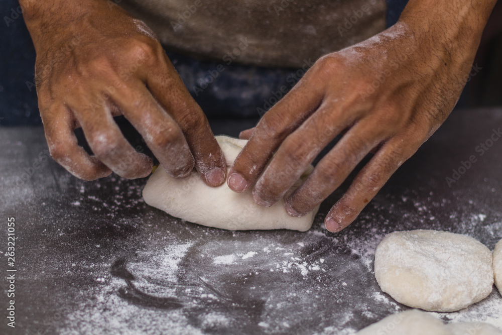 Male hands chef close-up, knead the dough, cook the dough on a dark background