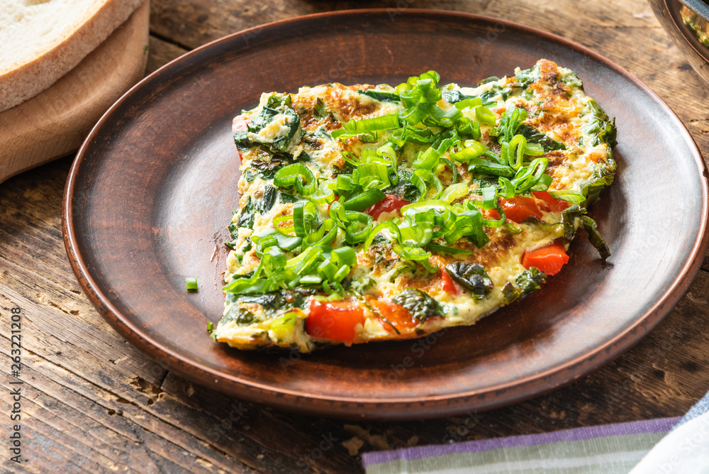 Home-made frittata with spinach and red pepper, sprinkled with spring onions on a plate and cutting board with bread, rustic style, close-up, top view Home-made frittata with spinach and red pepper, sprinkled with spring onions on a plate and cutting board with bread, rustic style, close-up, top view