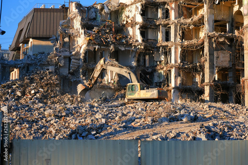 Building demolition with hydraulic excavator. Dismantle of destructed house ruins at bright sunsest © Arsenii