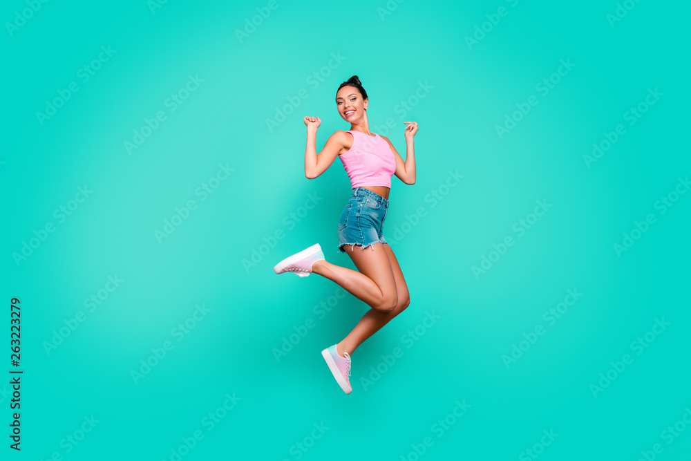 Full length side profile body size photo beautiful she her funny stylish trendy hairdo jump high lucky lottery wear casual pink tank-top jeans denim shorts isolated teal turquoise background