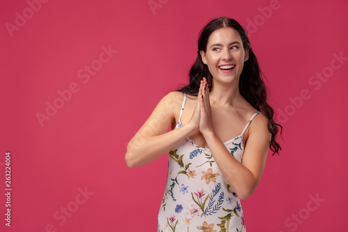 Portrait of a pretty young woman in a light dress standing on pink background in studio. People sincere emotions.