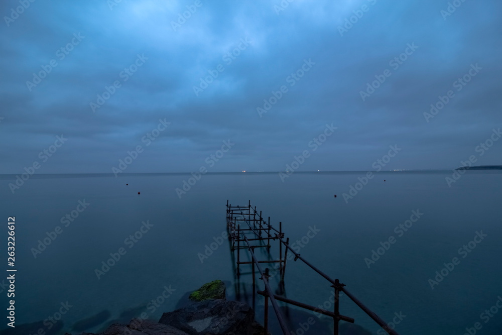 Marine landscape in the Blue hour with a metal construction that once was a bridge. From the shore of the Black Sea in Pomorie, Bulgaria.