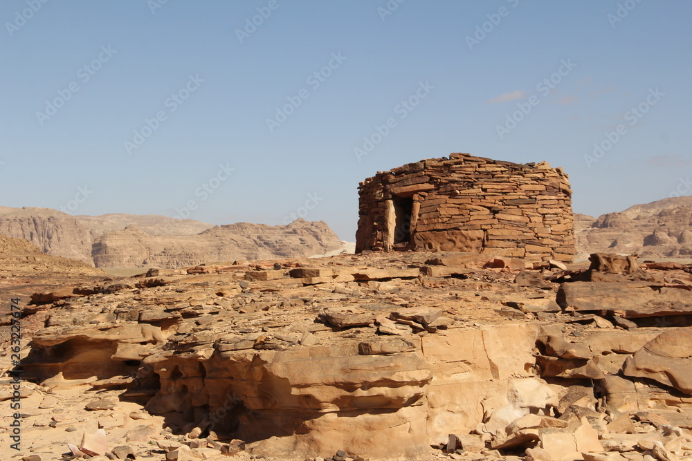 Bedouin stone structures in reddish-brown colors in the middle of the desert against a clear blue sky