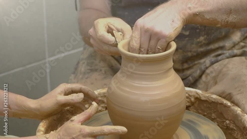 Two intertwined hands form a pot of clay on a potter's wheel. A male hand helps a woman's hands shape a clay shape.