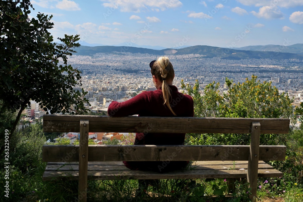 girl sitting on a bench on a high mountain overlooking the big city
