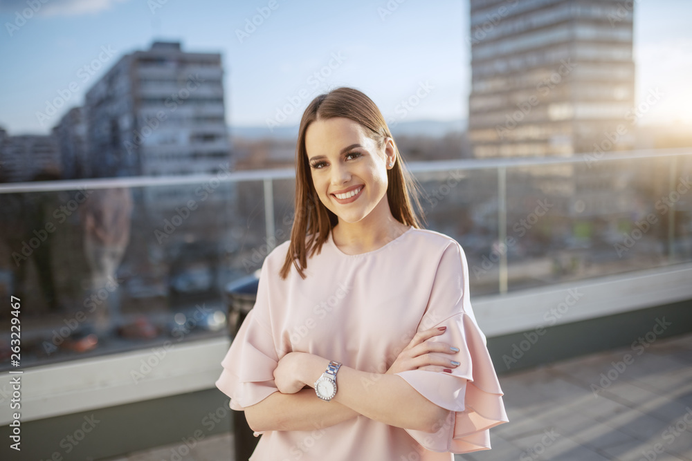 Fototapeta premium Portrait of gorgeous smiling Caucasian brunette dressed elegant standing with crossed arms on rooftop.