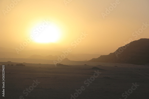 Sunset in the desert with dunes and rocky mountains
